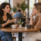 Dos mujeres conversan con atención y gestos tranquilos en una mesa.